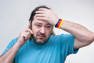 An adult man frustratedly holds his head during a heavy conversation on the phone. Bracelet in the colors of the German flag.
