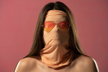 Portrait of unknown woman with face wrapped in fabric wearing glasses on a pink background