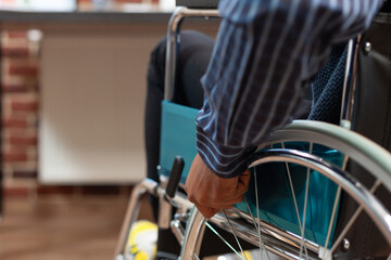 Obraz premium Focus on startup employee hand holding rim of wheelchair wheel to move around in red brick office. Closeup of african american man living with disability moving in workplace.