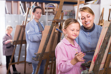 Smiling woman assistance girl during painting class at art studio