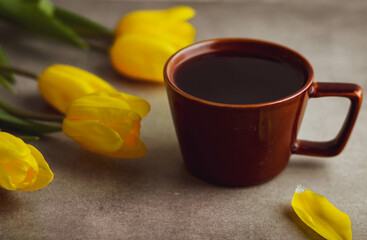 brown ceramic mug with black coffee, cookies and yellow tulips on a dark background. Greeting spring card