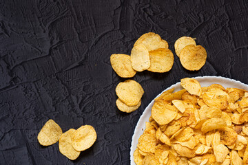 Delicious salty potato chips. Beer snacks on a black stone background. Top view. Free space for your text.