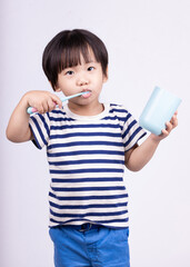 Cute little boy brushing teeth on white background.
