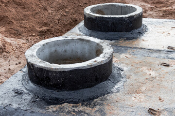 Installation of a reinforced concrete well for water supply and sewerage at the construction site. Well rings with cast iron hatch and construction tool.
