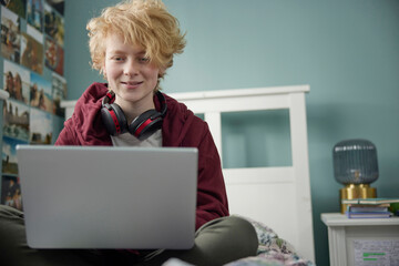 Teenage Girl With Wireless Headphones Working On Laptop In Bedroom At Home