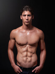 Herculean hunk. Studio shot of a handsome bare-chested young athlete standing against a black background.