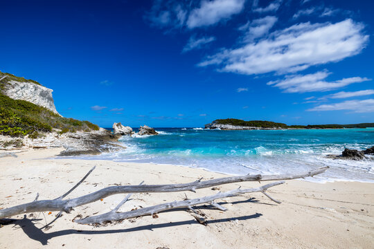 A secluded beach with a driftwood and turquoise sea next to the famous Colmbus Monument at Long Island, Bahamas