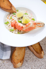 Close-up of seafood risotto served with a boiled kamchatka crab claw in a white plate, vertical shot