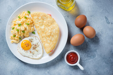 Chicken eggs cooked in different ways - scramble, omelet and fried eggs, top view on a light-blue stone background