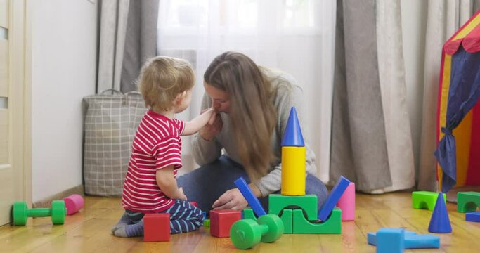 Mother with her son playing with colored cubes sitting on the floor at home. Family spends time together at home in children's room