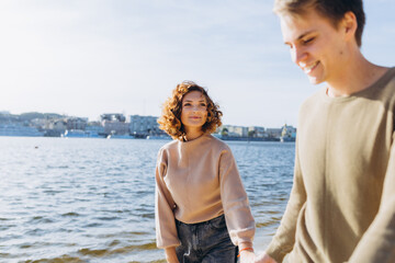 two young people in love running on the beach. They smile at each other. Beautiful couple holding hands. Beach. Feeling. Dress in a sweater