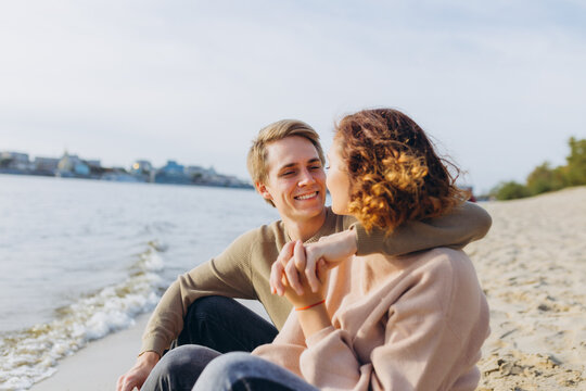 A loving couple has fun - they laugh, hug each other and enjoy a warm summer evening. Romantic couple sitting by the sea. Portrait of a guy hugging his girlfriend