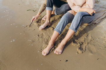 Male and female legs on the beach. The guy draws on the sand. Heart