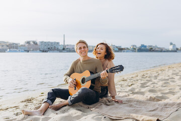 Fototapeta premium Happy couple in love. Stunning sensual portrait of a young couple. Young man playing guitar for his beloved girl.