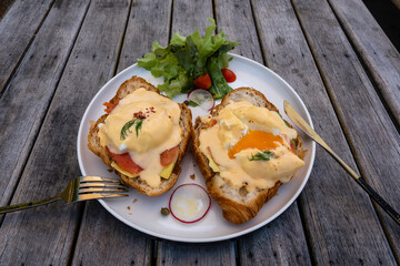 Croissant sandwich with poached egg, radish and salmon on plate in cafe
