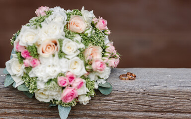 gold wedding rings lie on top of each other on a wooden board near a bouquet of roses close-up