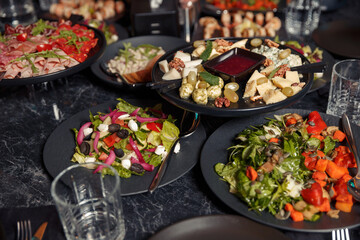 large black plates on a dark loft style table with fresh organic salads, cold cuts, prusciutto cheese. dinner at an expensive restaurant