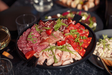 cold cuts on a large black plate with bacon, spicy sausage and prosciutto, a cold appetizer for beer or alcohol