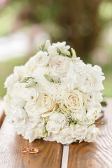 two wedding gold rings on a wooden table near a large bouquet of white beautiful roses