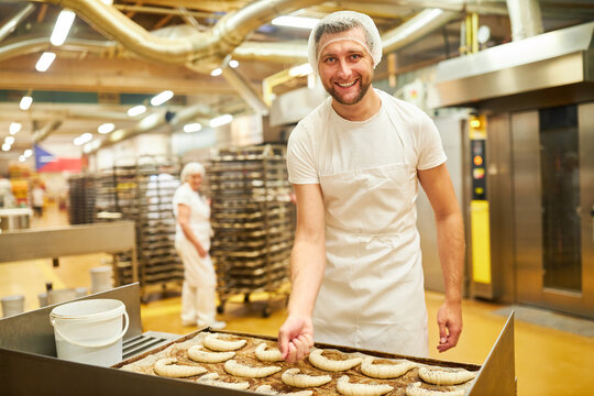 B&auml;cker Lehrling in der B&auml;ckerei bestreut Croissants mit Mohn
