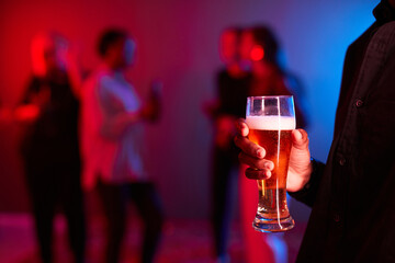 Close up of unrecognizable young man holding beer glass at party in neon lights, copy space