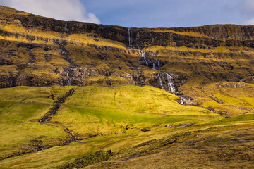 A waterfall flowing down a steep mountain slope on Streymoy Island, Saksun, Faroe Islands.