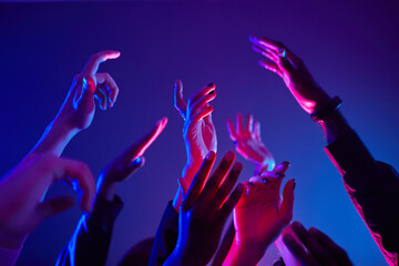 Close up of crowd dancing in club with hands up lit by neon lights, copy space - obrazy, fototapety, plakaty
