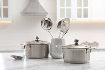 Stainless steel pots and kitchen utensils on white table indoors