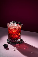 Summer cold cocktail drink with ice garnished with blackberry on dramatic violet