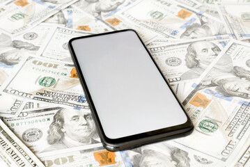 Smartphone mockup and money, mobile phone with white display, blank space for advertising lying on one hundred dollar bills. Business, finance and technology concept. Selective focus, low angle view