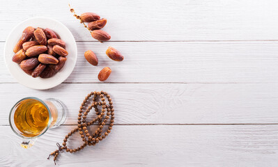Top view image of Ramadan Kareem decoration, dates fruit, tea and rosary beads on white wooden background.