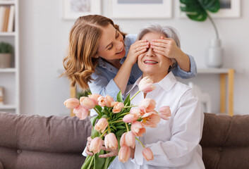 Delighted young woman congratulations mother with bouquet of fresh tulips