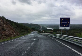 Frontera entre España y Portugal en un día lluvioso. Pequeña carretera en Pomarão (Portugal) con la señal de tráfico que indica que la frontera con España (portugués: Spanha) se encuentra a 1 kilómetr