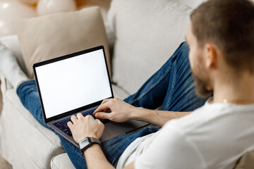 close-up of a man working on a laptop at home on the couch. no face.