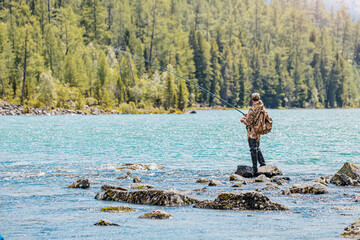 A man is fly fishing or spinning on a mountain lake. Recreational outdoor hobby and sport