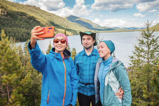 A Group Of Friends Taking Selfie Photos Against Stunning View Of An Idyllic Mountain Lake In A Nature Park In The Nordic Country