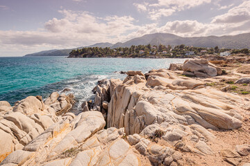 View of the picturesque scene of sea waves crashing on the rocks of a scenic island near resort town in Halkidiki region