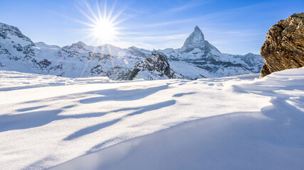 Alpine sunny winter landscape with a view of the Matterhorn, near Zermatt, in Switzerland. In the foreground an expanse of frozen snow shaped by the cold altitude wind.