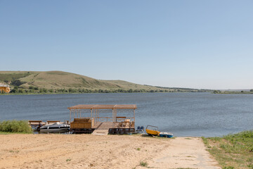 Fototapeta premium A small sandy beach on a pond with a pier and pleasure boats. Eastern Europe, summer, clear weather.