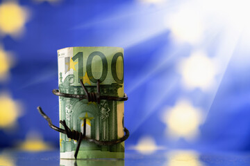 European Union currency wrapped in barbed wire against flag of EU as symbol of economic sanctions...