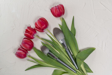 Bouquet of pink tulip flowers on a gray background with a set of makeup brushes