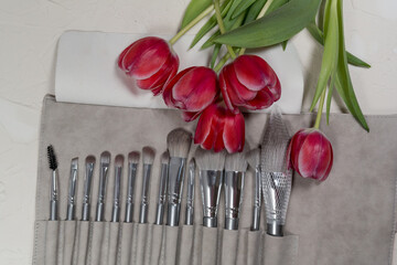 Fototapeta na wymiar Bouquet of pink tulip flowers on a gray background with a set of makeup brushes