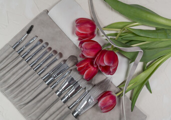 Bouquet of pink tulip flowers on a gray background with a set of makeup brushes