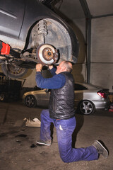 Fototapeta na wymiar mechanic on his knees in workshop pulling back a drive shaft of car in suspension