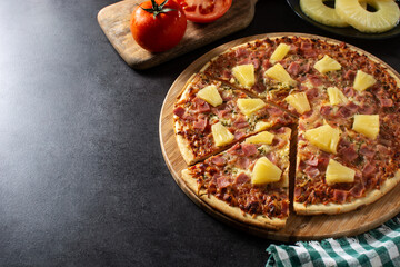 Hawaiian pizza with pineapple,ham and cheese on black stone. Copy space