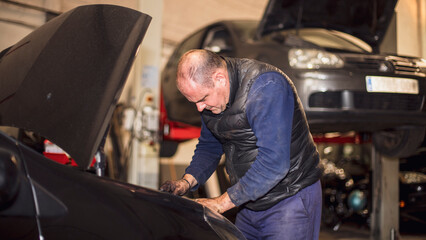 Mechanic supervising interior of car with car hood open in workshop