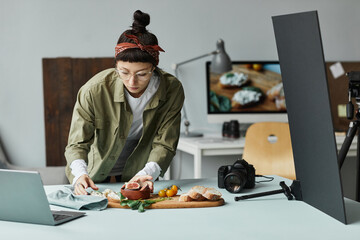 Front view portrait of female food photographer arranging gourmet setup with props, digital creator...