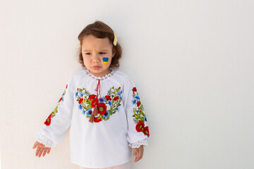 Little Ukrainian girl in an embroidered shirt on a white background. A little girl in national Ukrainian clothes - vyshyvanka. Little Ukrainian girl with a patriotic flag.