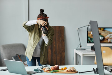 Portrait of female food photographer taking pictures while working in home studio setup, copy space