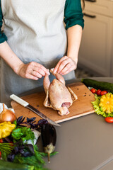 A girl is cutting up a chicken on a wooden plank. Next to it are some vegetables. The process of cooking chicken tobacco